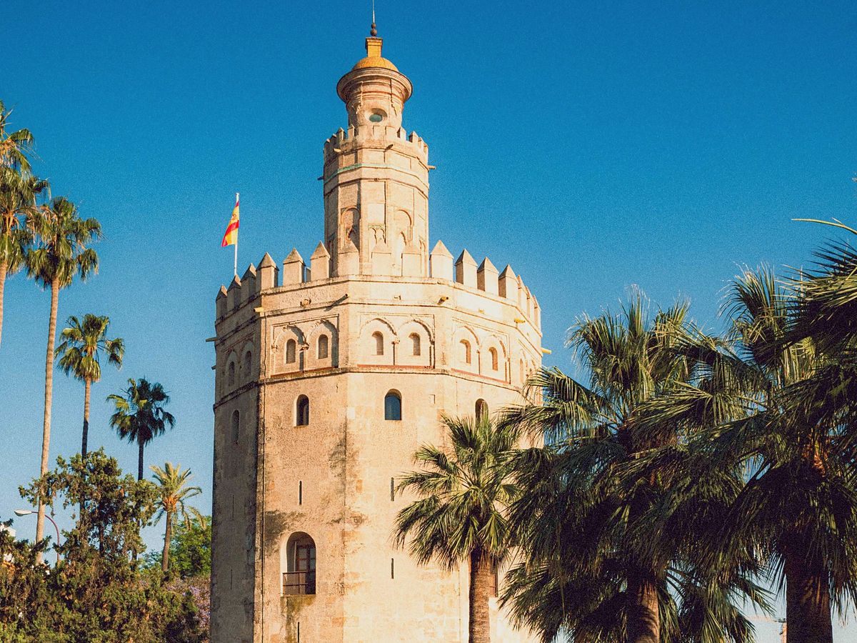La Torre del Oro de Sevilla entre palmeras bajo un cielo azul.