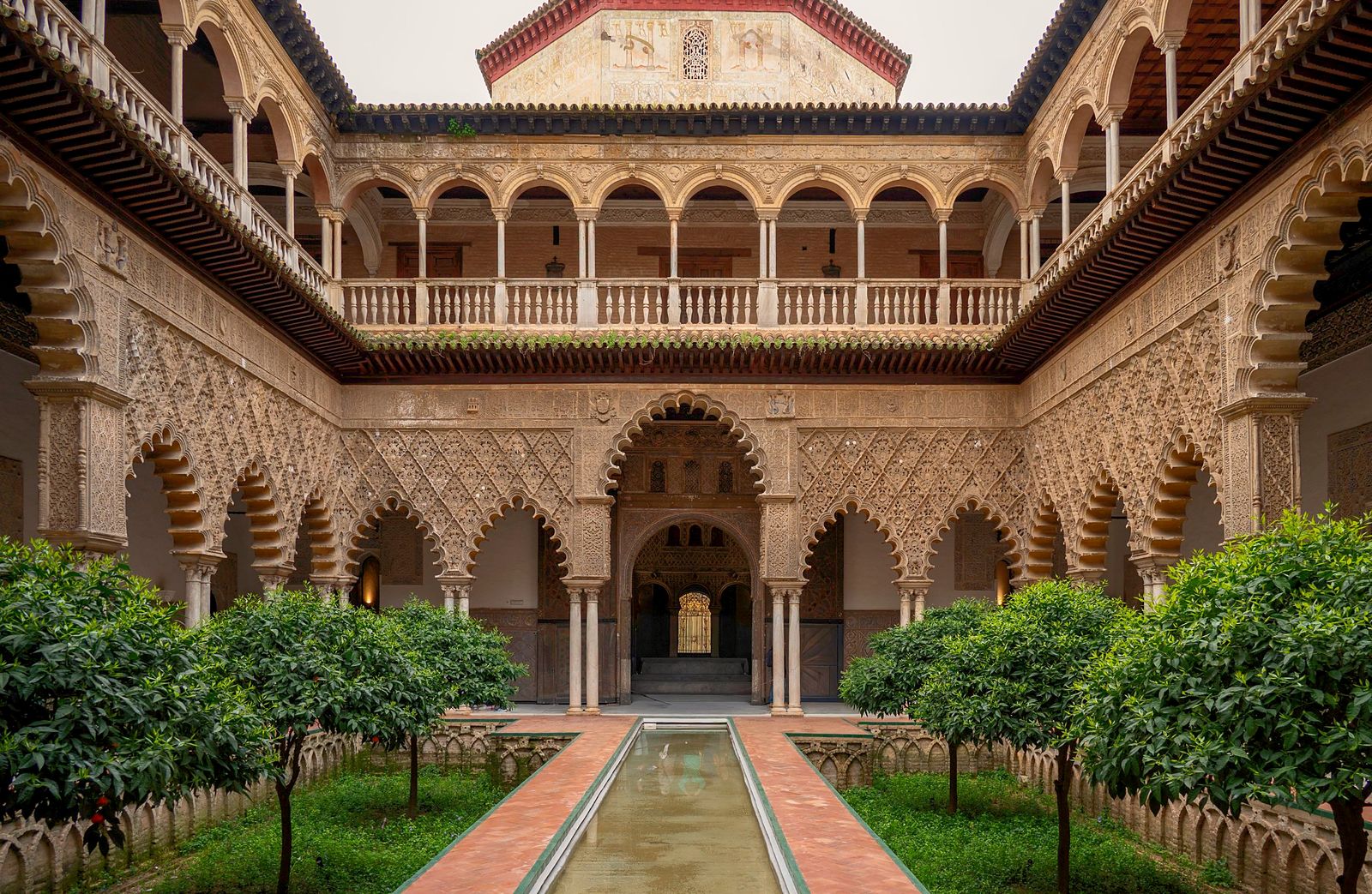 Patio de las Doncellas del Real Alcázar de Sevilla, con naranjos y un estanque central.