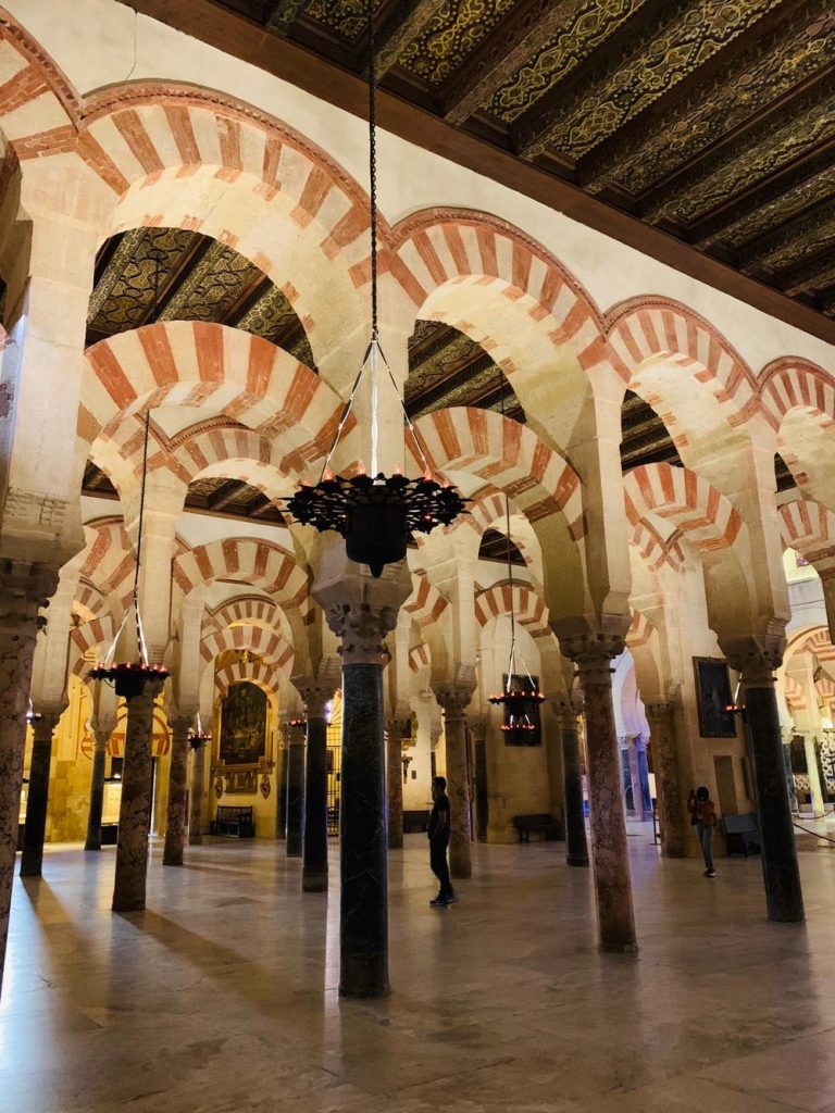 Red-and-white horseshoe arches and marble columns inside the Mosque-Cathedral of Córdoba, with a hanging lamp.
